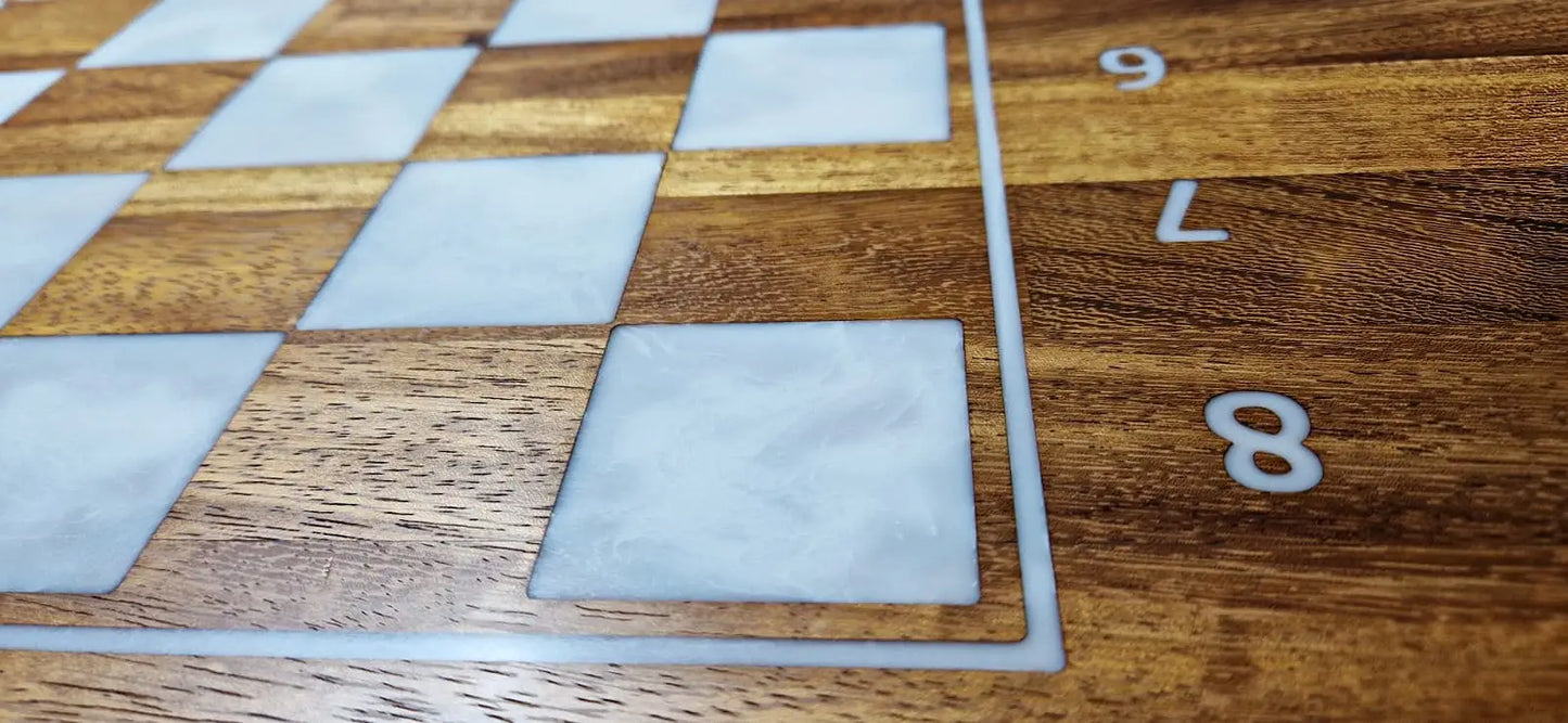 A detailed close-up of a ChessboArt bughouse chess table, showing the algebraic notation on the Iroko wood border. The image highlights the deep grain of the Iroko squares next to the smooth, pearlescent white squares.