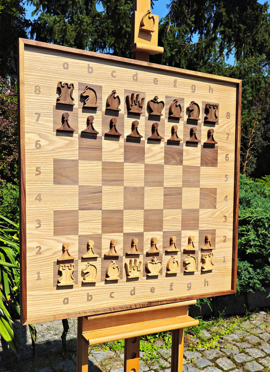 The ChessboArt 800 large wooden chess board displayed on an easel outdoors. Crafted from American walnut and heartwood ash, this 800x800mm board features a unique minimalist design with a seamless transition and no inner border separating the squares from the coordinate margins. Set up with solid wood flat profile pieces.