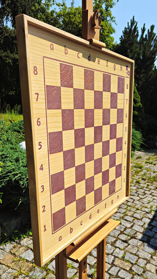 ChessboINK wall-mounted chessboard made of natural ash wood with pink painted squares, displayed outdoors on a wooden easel.