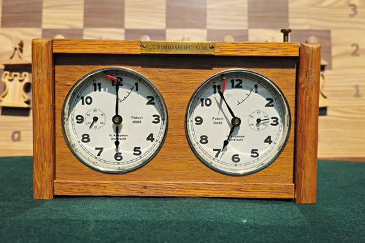 Straight-on front view of a vintage 1960s Koopman wooden chess clock. The image clearly shows the two analog dials with 'H. Koopman Dordrecht' text, the brass 'C. Kommandeur-Klok' plaque, and the top push buttons.