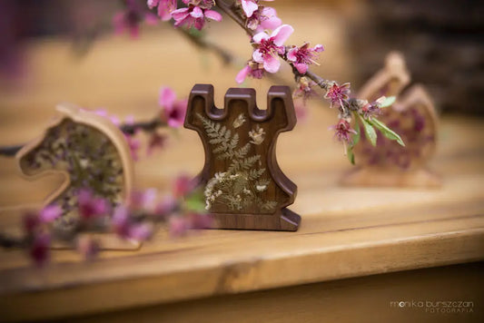 A ChessboArt king piece topped with a cross, its heart-shaped body filled with a pressed daisy, fern, and purple petals set in resin by Tollini, standing against a dark green background