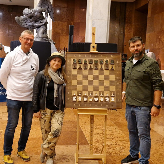Michał Fudalej and Grandmaster Judit Polgár standing next to a vertical magnetic chessboard at a Hungarian art gallery event.