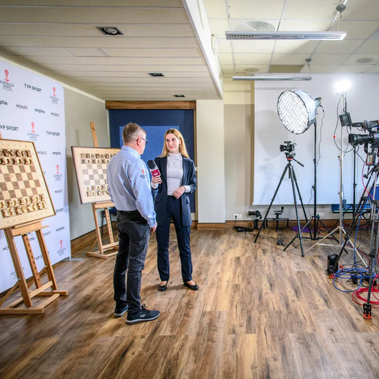 Magdalena Budkiewicz interviewing IM Grzegorz Masternak from GKS Hetman Katowice at the Superliga Rapid tournament. Professional studio lighting and cameras filming against a sponsor wall decorated with two ChessboArt wooden hanging chess boards.