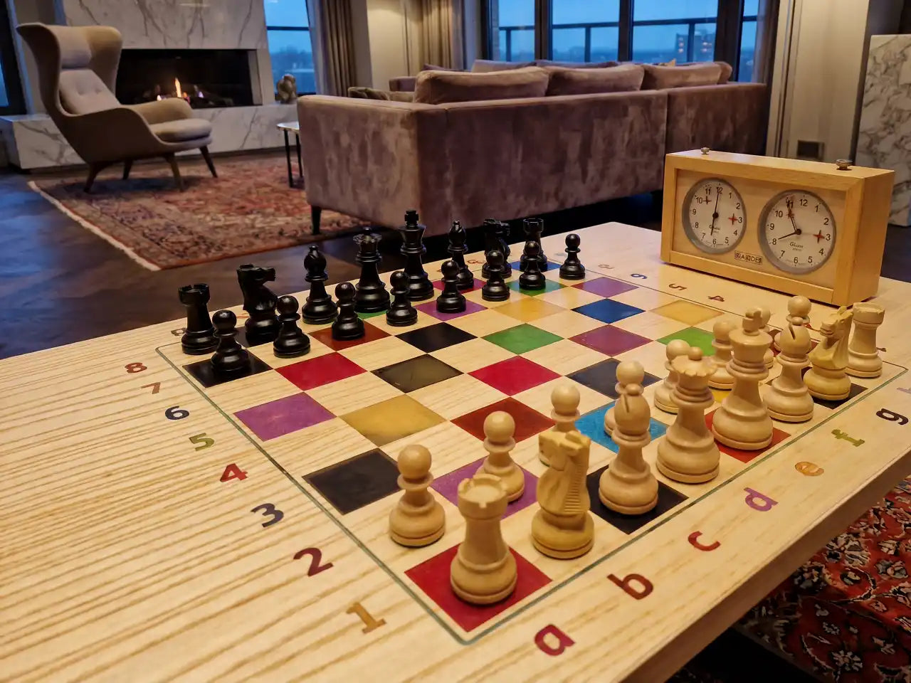A handcrafted, colorful solid wood chess table with professional pieces and a vintage clock, displayed in a modern luxury living room with a fireplace.