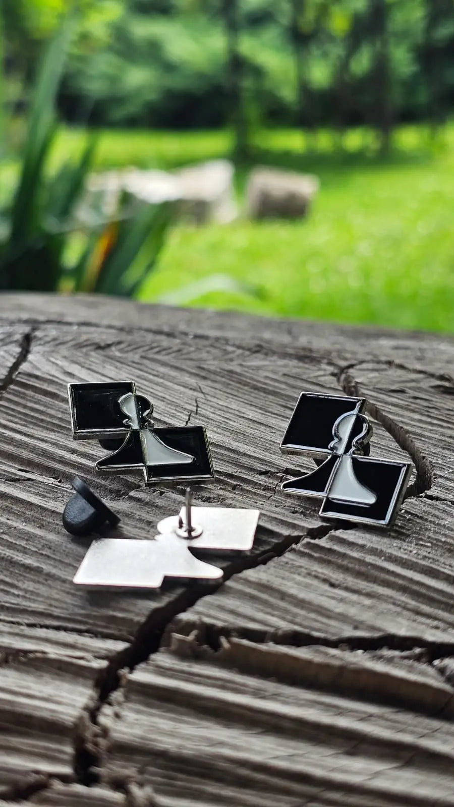 Two ChessboArt enamel pins placed on a rustic wooden stump outdoors