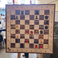Wall chess board with red and dark pieces set up as a chess puzzle, task written above in marker