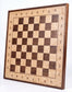 Angled view of the ChessboArt 800 wall-mounted chessboard, primarily made of light ash wood with dark contrasting walnut squares, showcasing the natural wood grain.