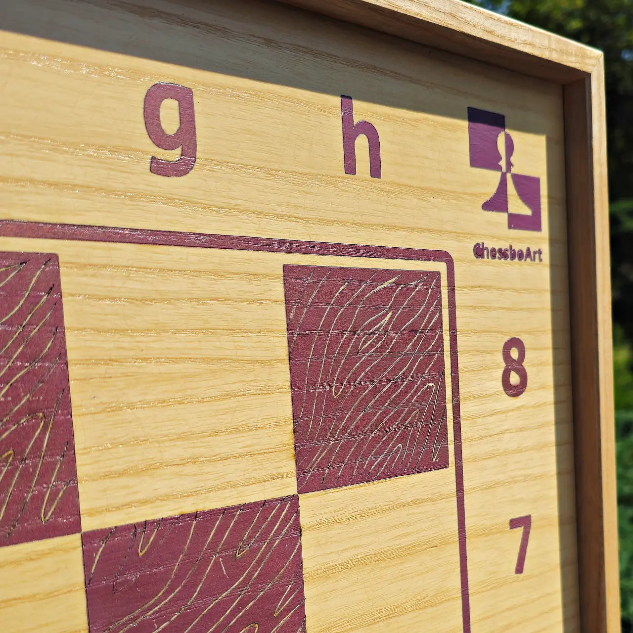 Macro shot of the top right corner of the pink ash wood chessboard, featuring the purple ChessboArt logo, coordinate numbers 7 and 8, and the edge of the natural ash wood frame.