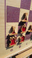 Angled close-up of the ChessboINK wall-mounted chessboard made of pink-painted ash wood, featuring unique flat wooden chess pieces with vibrant red epoxy resin fillings casting shadows in the sunlight.