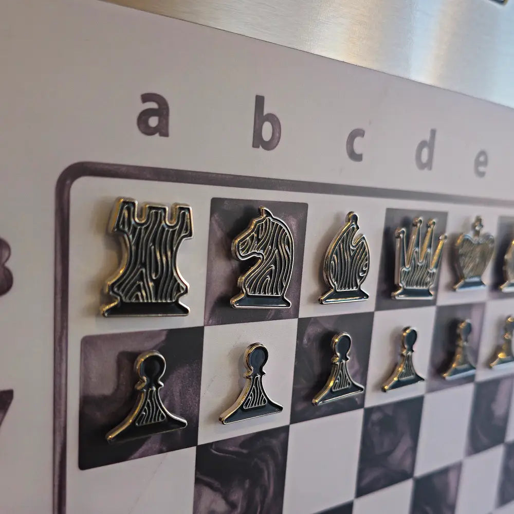 Black and gold enamel chess pieces shaped like pin badges on the Epoxy Ivory magnetic board