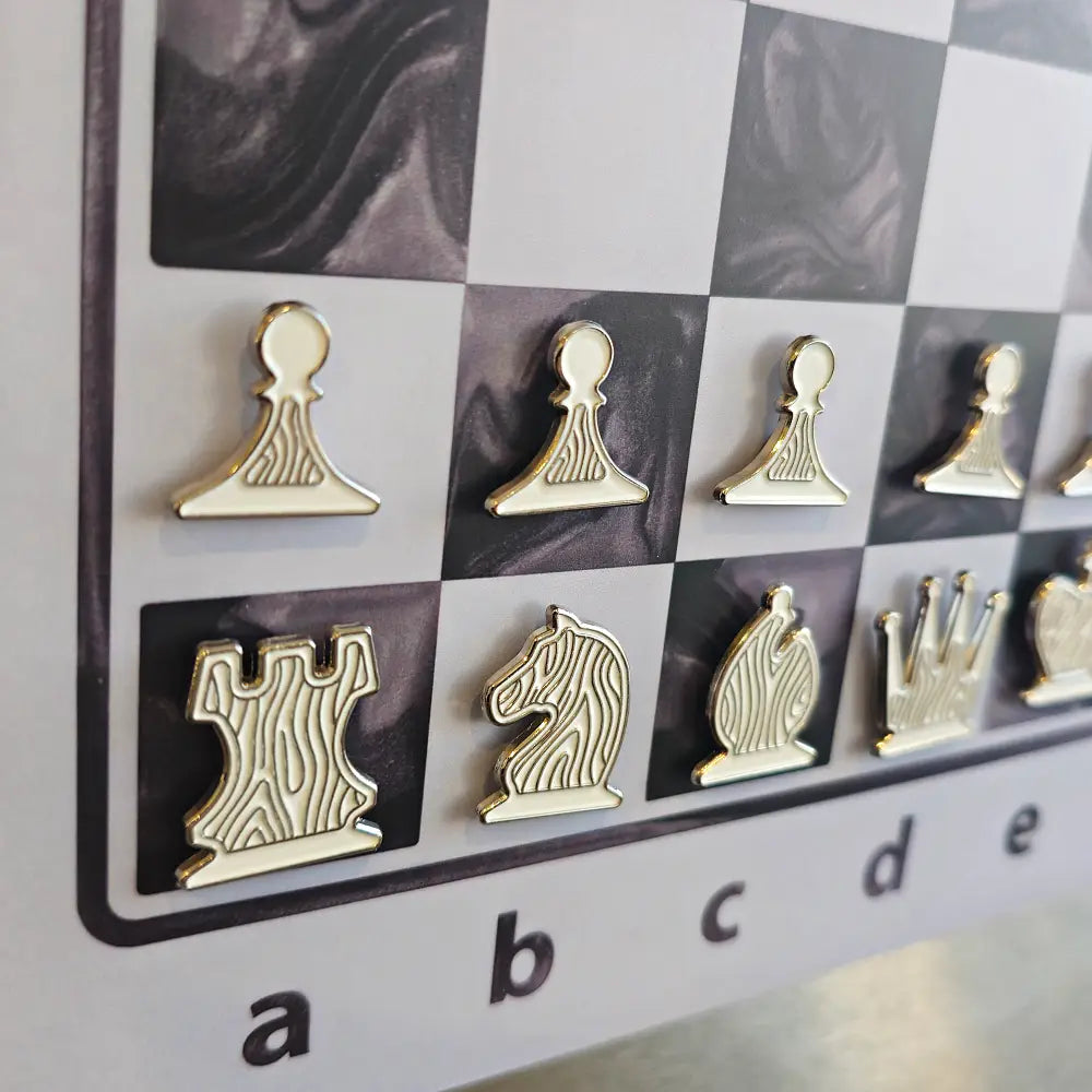 Cream and gold enamel chess pieces shaped like pin badges on the Epoxy Ivory magnetic board