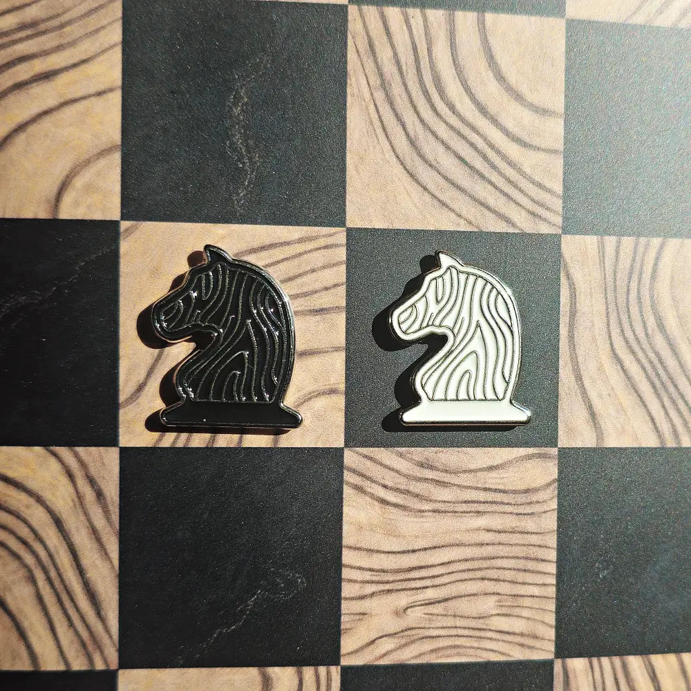 Black and cream enamel knight chess pieces shaped like pin badges on the Ivory Grain magnetic board