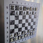 Close-up of the Epoxy Ivory magnetic chessboard on a fridge, enamel pin chess pieces in starting position