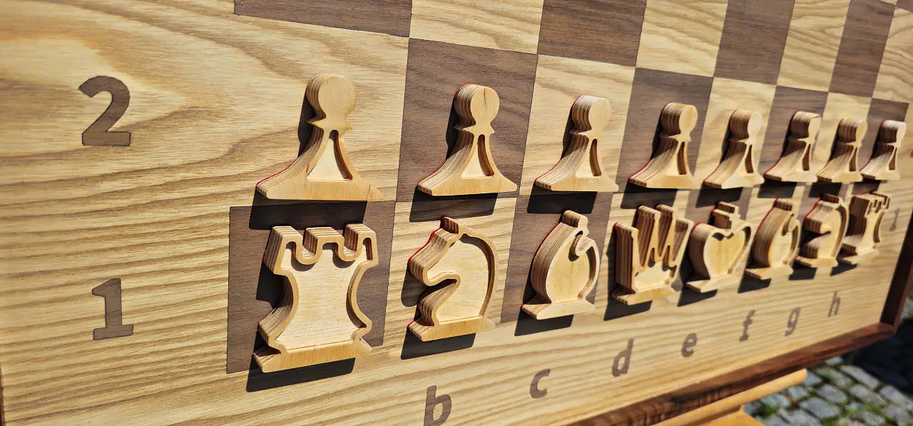 Close-up angled view of the white plywood chess pieces on the ChessboArt 800 wall board. The macro shot highlights the open, unfilled design of the layered plywood figures, standing on the seamless heartwood ash and American walnut playing surface.