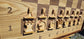 Close-up angled view of the white plywood chess pieces on the ChessboArt 800 wall board. The macro shot highlights the open, unfilled design of the layered plywood figures, standing on the seamless heartwood ash and American walnut playing surface.