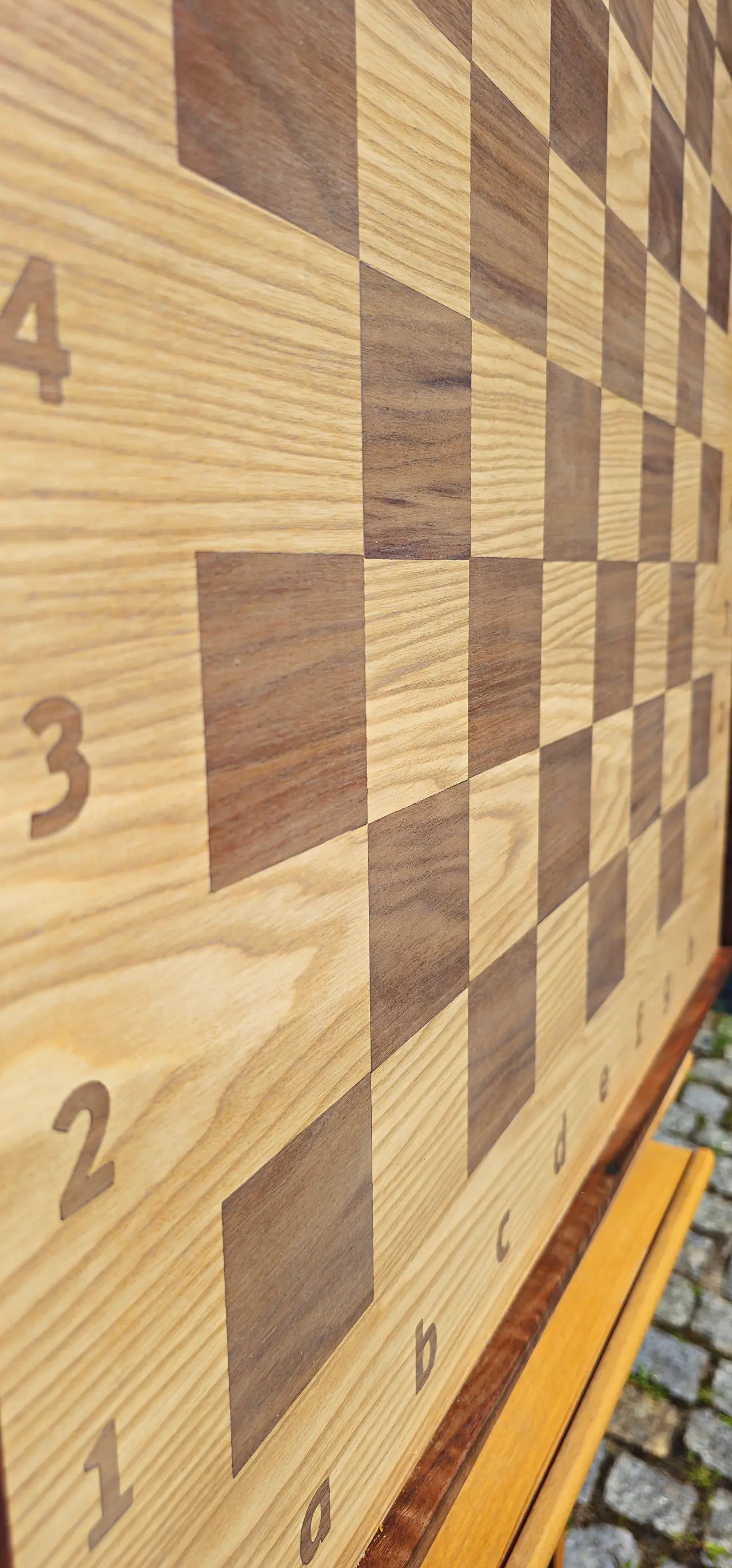Extreme close-up view of the empty ChessboArt 800 wooden chessboard. The macro angle beautifully captures the rich wood grain of the heartwood ash and American walnut squares, highlighting the seamless transition to the margins and the precise alphanumeric coordinates.