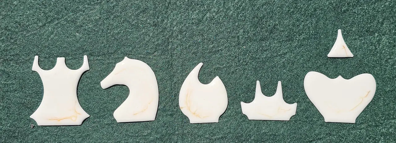 Five chess piece inlay shapes in white and gold resin arranged in a row: rook, knight, bishop, queen, king
