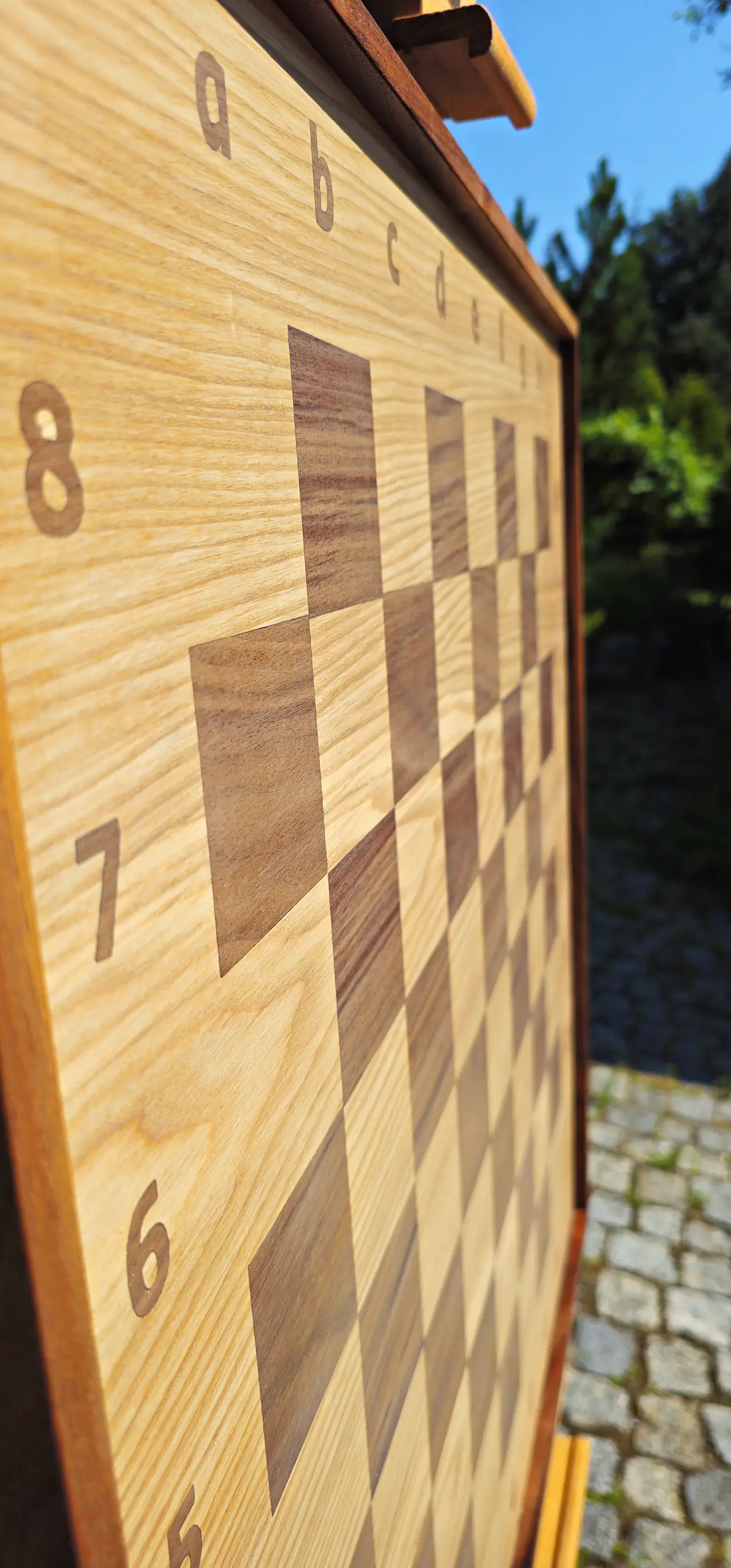 Low angle close-up of the ChessboArt 800 empty wooden chessboard. This dynamic perspective emphasizes the smooth, flat surface where the heartwood ash and American walnut playing squares blend seamlessly into the numbered outer margins.
