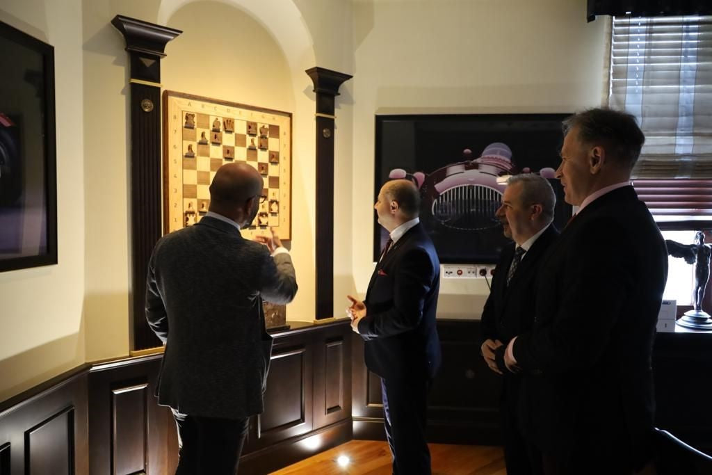 group of men in suits observing a vertical chessboard in an elegant interior, showcasing a refined and classic design