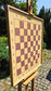 ChessboINK wall-mounted chessboard made of natural ash wood with pink painted squares, displayed outdoors on a wooden easel.