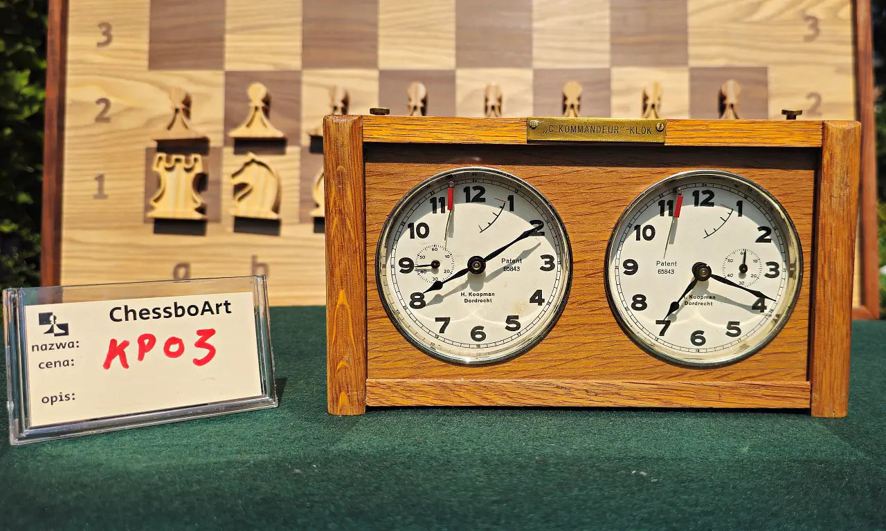 Front view of a working vintage wooden chess clock from the 1960s, model KP03. The clock features two analog dials by H. Koopman Dordrecht and a brass C. Kommandeur-Klok plaque, displayed next to a ChessboArt identification card.