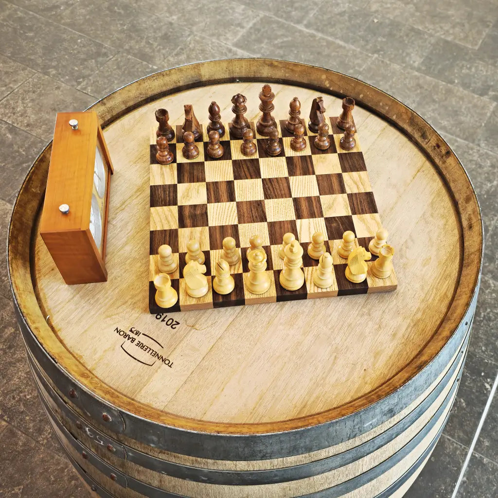 Wooden chess set with pieces mid-game and a chess clock resting on a wine barrel at Le Vignoble Torpez, Saint-Tropez